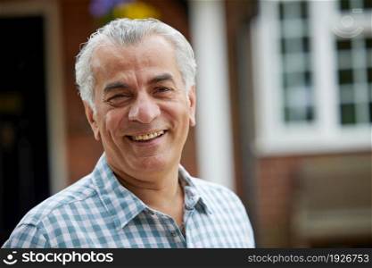 Portrait Of Mature Man Standing In Garden In Front Of Dream Home In Countryside