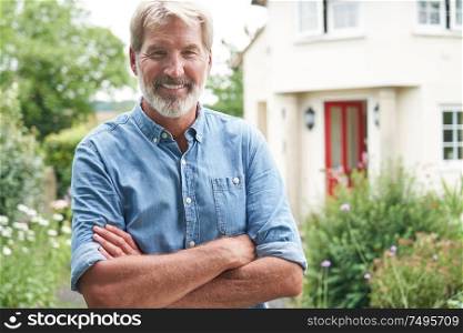 Portrait Of Mature Man Standing In Garden In Front Of Dream Home In Countryside