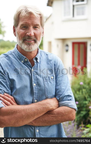 Portrait Of Mature Man Standing In Garden In Front Of Dream Home In Countryside