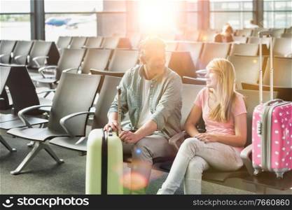Portrait of mature man talking to her daughter while waiting and sitting in airport with yellow lens flare