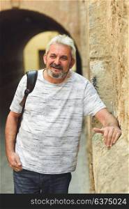 Portrait of mature man with grey hair smiling in urban background. Senior male with white hair and beard wearing casual clothes.
