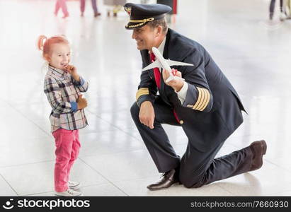 Portrait of mature pilot holding airplane toy while playing with cute little girl in airport