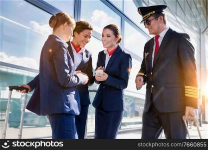 Portrait of mature pilot talking with young attractive flight attendants during arrival in airport