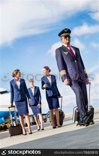 Portrait of mature pilot walking with three young beautiful flight attendants against airplane in airport