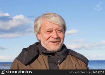 Portrait of mature smiling man with grey hair at the Baltic sea in autumn day.