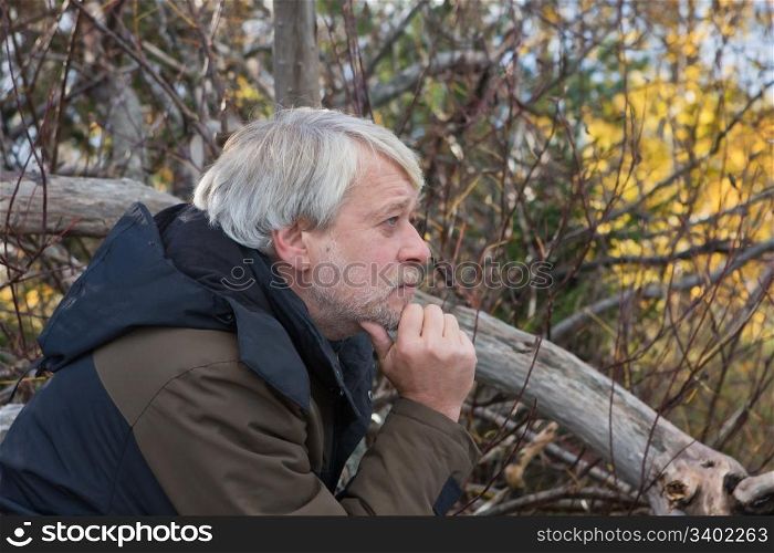 Portrait of mature thoughtful man with grey hair in forest in autumn day.