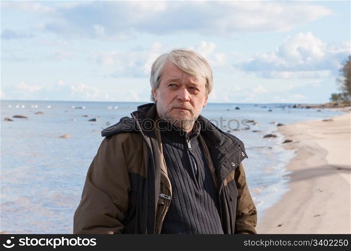 Portrait of mature thoughtful poor man with grey hair at the Baltic sea in autumn day.
