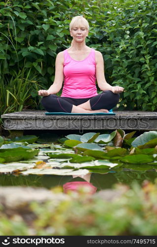Portrait Of Mature Woman In Yoga Position On Wooden Jetty By Lake