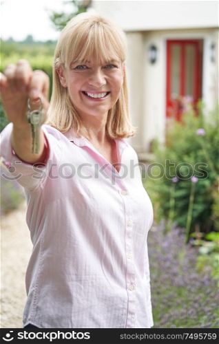 Portrait Of Mature Woman Standing In Garden In Front Of Dream Home In Countryside Holding Keys