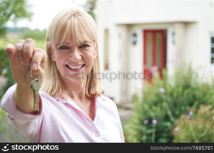 Portrait Of Mature Woman Standing In Garden In Front Of Dream Home In Countryside Holding Keys