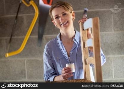 Portrait Of Mature Woman Upcycling Furniture In Workshop At Home Painting Wooden Chair