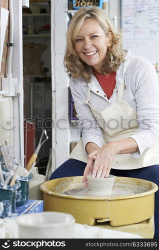 Portrait Of Mature Woman Working At Potters Wheel In Studio