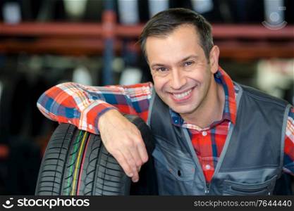portrait of mechanic in garage with new car tyre