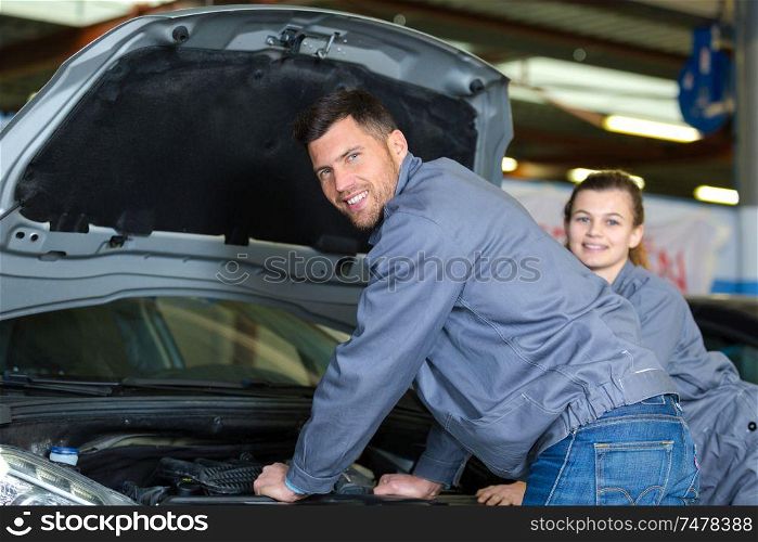 portrait of mechanic with young female colleague stood by car