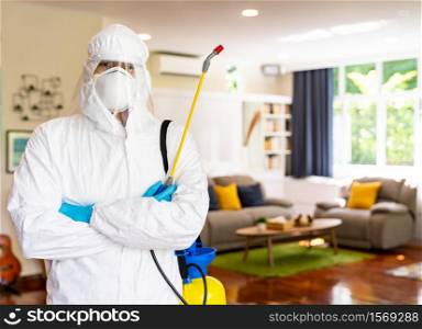 Portrait of medical staff in personal protective equipment PPE suit with coronavirus COVID-19 disinfectant spray with living room background. Delivery health care hygiene and disinfection concept