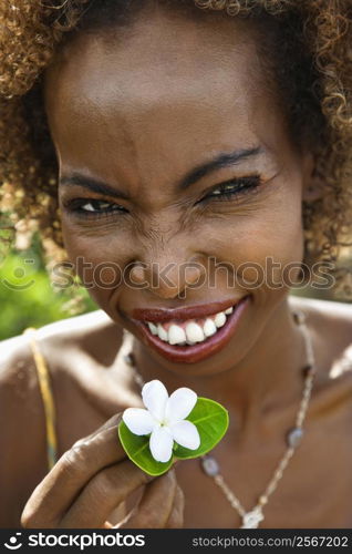 Portrait of mid-adult African American female squinting and holding jasmine flower.