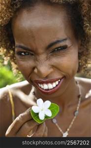 Portrait of mid-adult African American female squinting and holding jasmine flower.