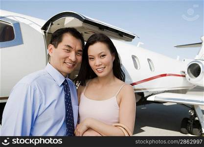 Portrait of mid-adult Asian business couple standing in front of private airplane.