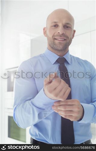 Portrait of mid adult businessman buttoning sleeve at home