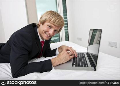 Portrait of mid adult businessman using laptop in bed at home