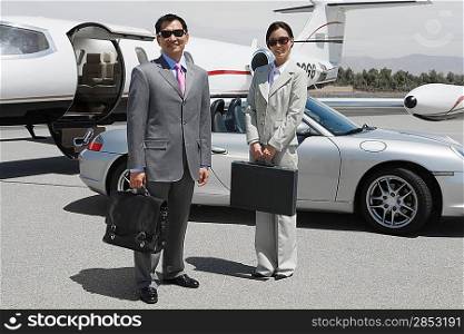 Portrait of mid-adult businesswoman and mid-adult businessman standing in front of private plane on landing strip.