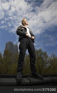 Portrait of mid-adult Caucasian male punk standing on ledge with skyline in background.