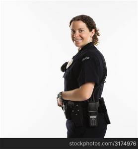 Portrait of mid adult Caucasian policewoman standing with hand on gun holster looking over shoulder at viewer smiling.
