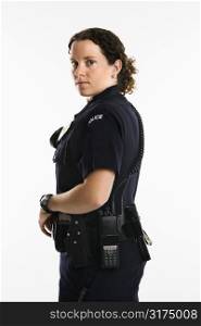 Portrait of mid adult Caucasian policewoman standing with hand on gun holster looking over shoulder at viewer.