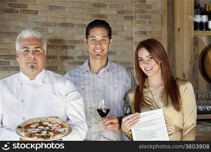 Portrait of mid adult chef holding pizza with young couple