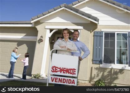 Portrait of mid-adult couple in front of new house, children (6-9) in background