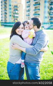 Portrait of mid adult couple kissing toddler daughter in park