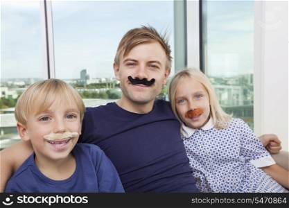 Portrait of mid adult man and children with artificial mustache at home