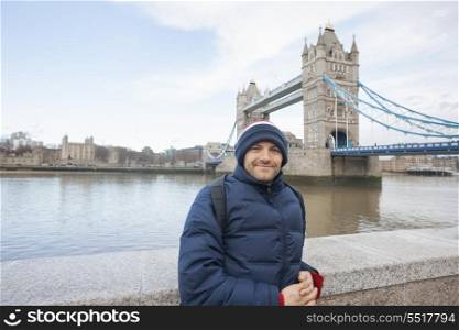 Portrait of mid adult man in warm clothing standing in front of tower bridge; London; UK