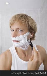 Portrait of mid-adult man shaving in bathroom