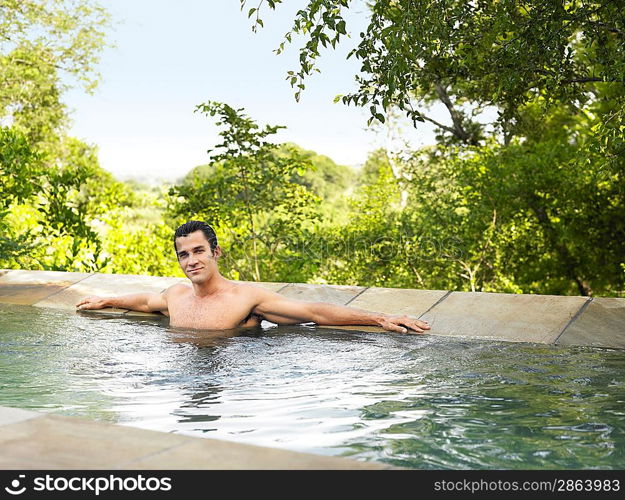 Portrait of mid adult man sitting in pool arms outstretched