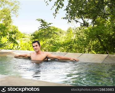 Portrait of mid adult man sitting in pool arms outstretched