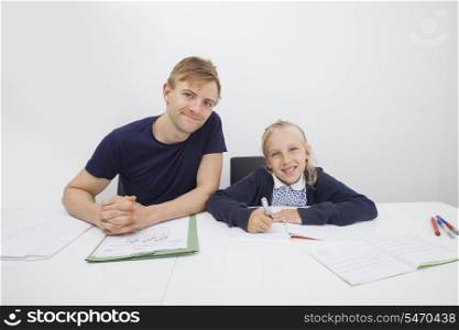 Portrait of mid adult man sitting with daughter studying at table