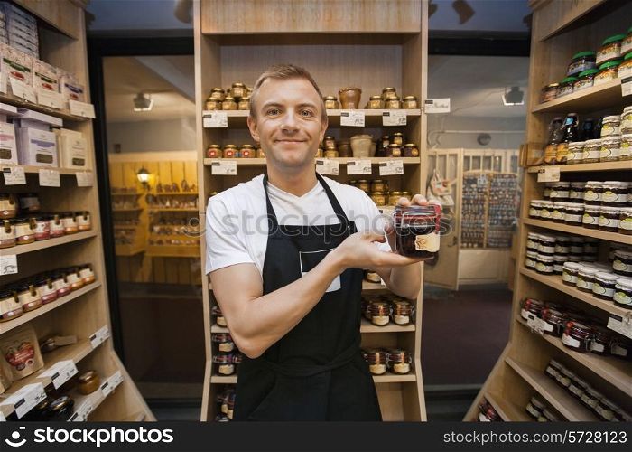 Portrait of mid adult salesman holding jar of jam in grocery store