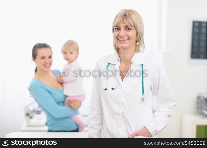 Portrait of middle age pediatric doctor and mother with baby in background