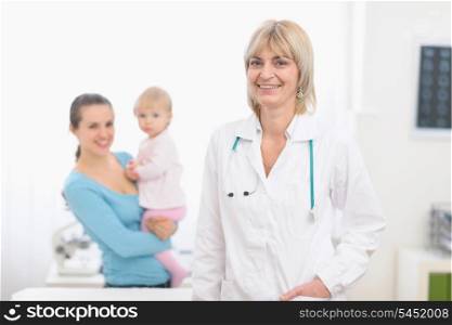 Portrait of middle age pediatric doctor and mother with baby in background