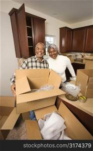 Portrait of middle-aged African-American couple with moving boxes in kitchen.