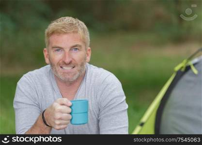 portrait of middle-aged man holding cup on camping trip