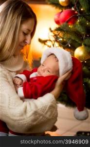 Portrait of mother and baby in Santa costume at fireplace