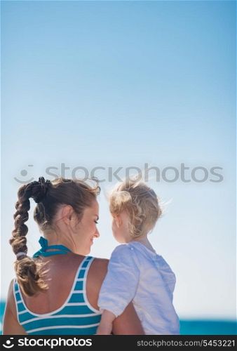 Portrait of mother and baby on beach. Rear view