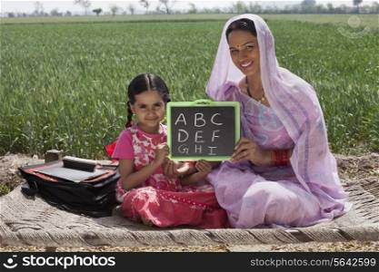 Portrait of mother and daughter holding a writing slate with alphabets written on it