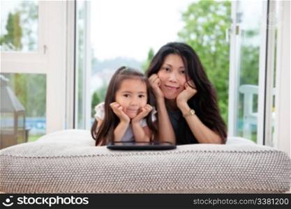 Portrait of mother and daughter lying on couch with digital tablet