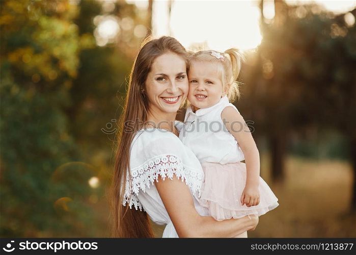 portrait of mother and daughter. mother holds a little girl in her arms on the background of a meadow. little girl with two tails. portrait of mother and daughter. little girl with two tails. mother holds a little girl in her arms on the background of a meadow