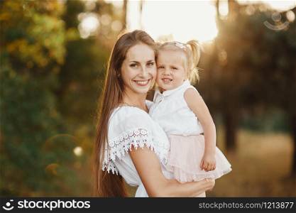 portrait of mother and daughter. mother holds a little girl in her arms on the background of a meadow. little girl with two tails. portrait of mother and daughter. little girl with two tails. mother holds a little girl in her arms on the background of a meadow