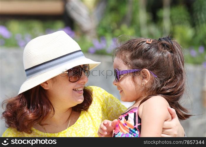 Portrait of mother and daughter outdoors looking each other in sumertime. Focus on the little girl