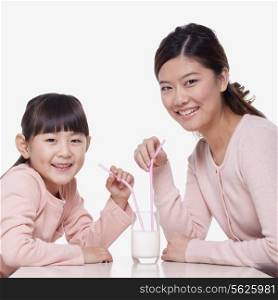 Portrait of mother and daughter sharing a glass of milk, studio shot